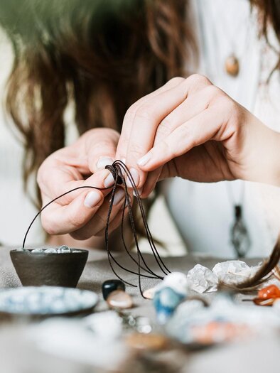 A person carefully threads a string through a wire. Various pieces of jewelry and materials are lying on the table. | © adobe stock foto