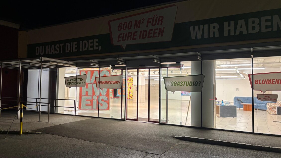 Ein Geschäft mit großen Fenstern und einem transparenten Eingangsbereich. Es ist nachts und die Innenbeleuchtung ist eingeschaltet. | © MitteninZeltweg
