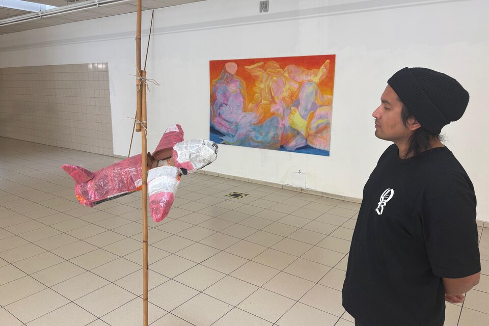 Eine Person steht in einem Raum und schaut auf ein hängendes, rosa Fischkunstwerk. Im Hintergrund ist ein buntes Gemälde zu sehen. | © manifestderleere