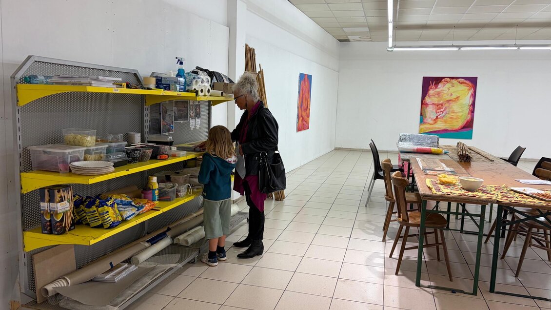 Ein kreativer Raum mit Regalen voller Bastelmaterialien. Eine Frau steht mit einem Kind an einem Tisch in einem hellen, offenen Atelier. | © Anna Khodorkovskaya