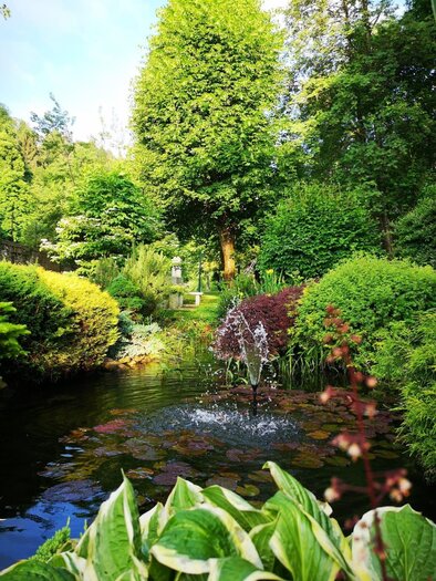 Ein schöner Garten mit üppigem Grün und bunten Pflanzen. Im Vordergrund sprudelt ein kleiner Brunnen in einem Teich. | © TV Südsteiermark