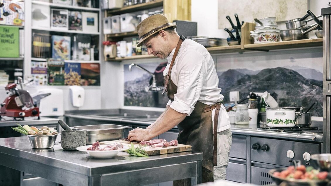 Ein Koch arbeitet konzentriert in einer modernen Küche. Er bereitet frische Zutaten und Fleisch für ein Gericht vor. | © Löke