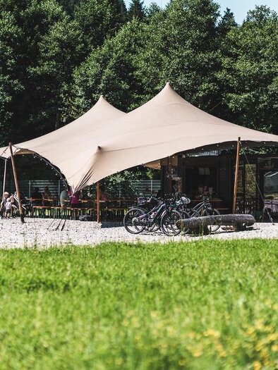 A cozy snack stand with large red awnings. Wooden tables and benches invite you to linger in beautiful nature. | © Auszeit Ausseerland