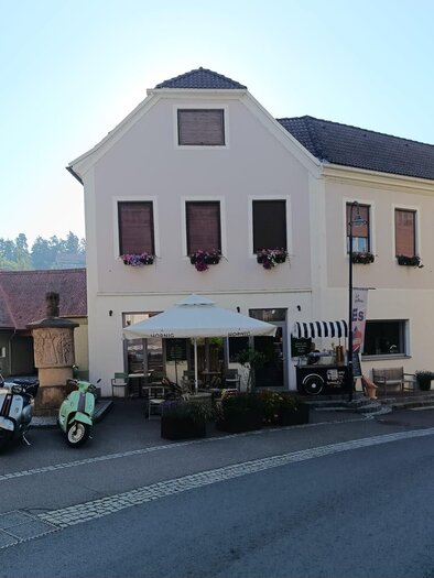 A charming building on a street, surrounded by trees. In front of the establishment are a few vehicles and a sun umbrella. | © Jürgen Atschko