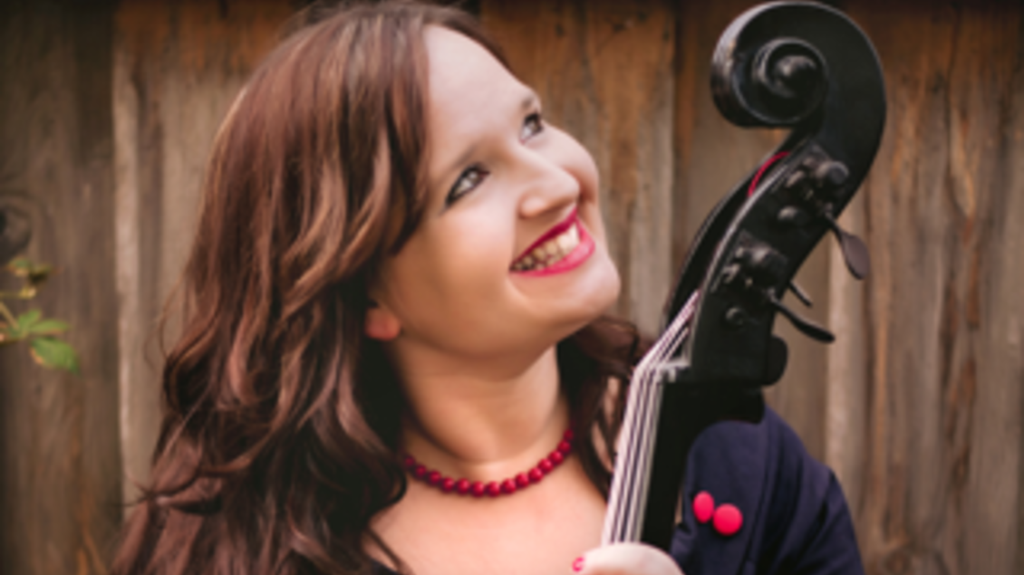 Eine lächelnde Frau hält ein Cello. Im Hintergrund ist ein holziger Zaun zu sehen. | © Jan Balaz