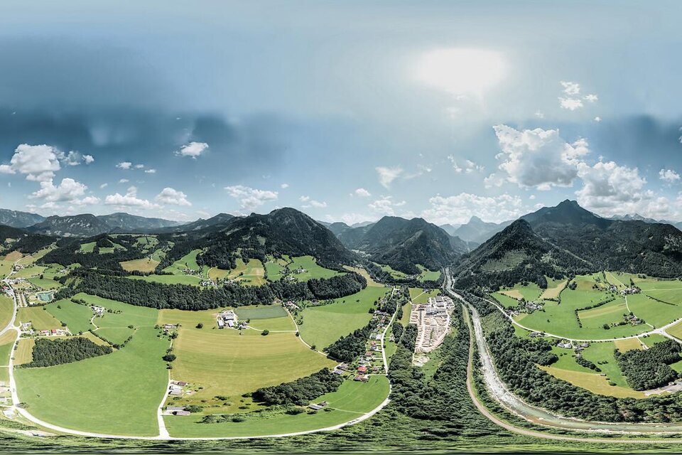 Eine weitläufige Landschaft mit grünen Wiesen und sanften Hügeln unter einem klaren Himmel. Im Hintergrund sind Berge und Wolken sichtbar. | © Thomas guggenberger