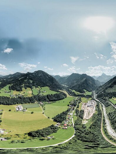Eine weitläufige Landschaft mit grünen Wiesen und sanften Hügeln unter einem klaren Himmel. Im Hintergrund sind Berge und Wolken sichtbar. | © Thomas guggenberger