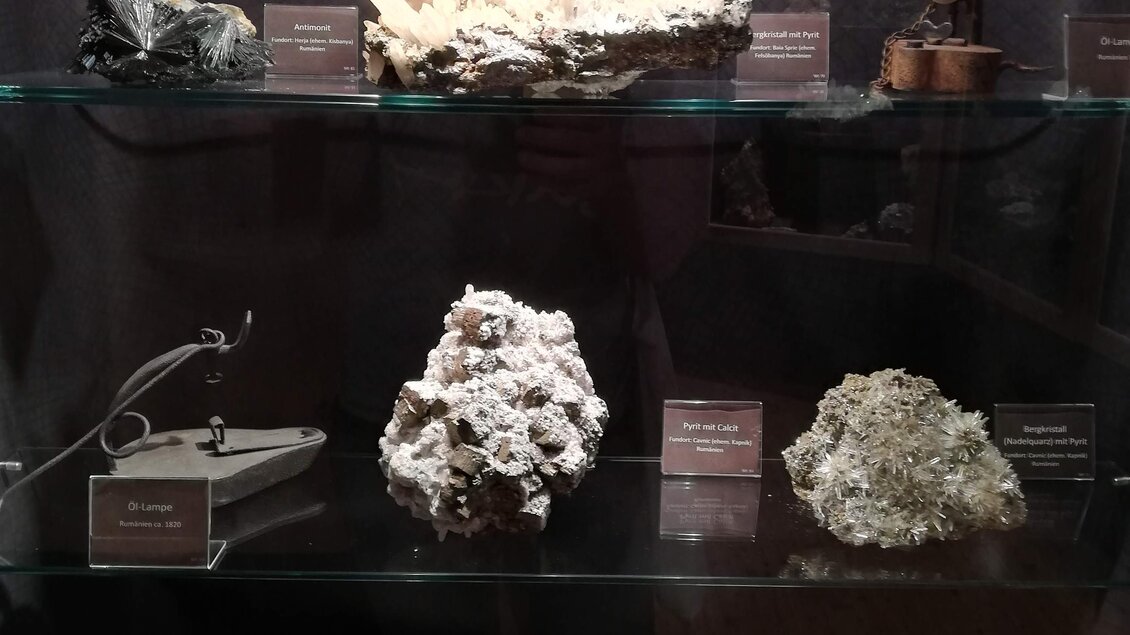 Eine Ausstellung mit verschiedenen Mineralien und Kristallen auf Glasregalen. Die Objekte sind beschriftet und zeigen unterschiedliche Formen und Farben.