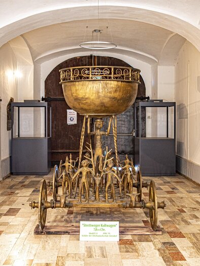An elegant artwork in a museum, displayed in a glass case. In the background, historical walls and a sculpture are visible. | © Erlebnisregion Murtal