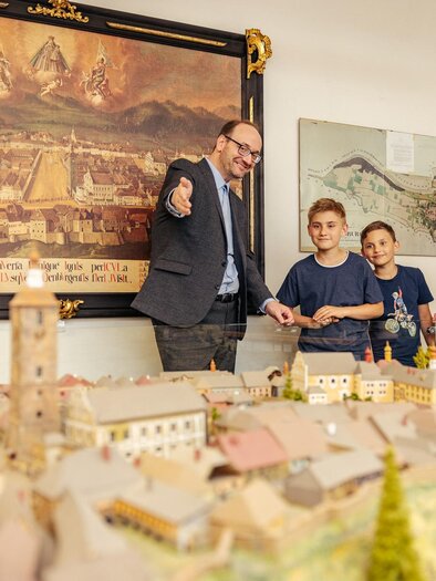 Eine Gruppe von Menschen steht um ein detailliertes Modell eines historischen Ortes. Im Hintergrund hängen Bilder und technische Geräte. | © Erlebnisregion Murtal