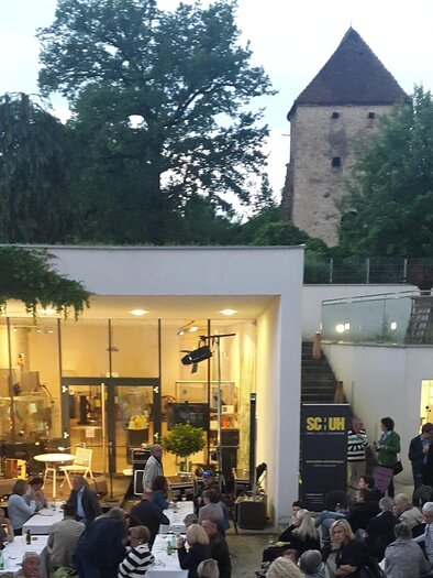 Eine Veranstaltung im Freien mit vielen Menschen und Tischen. Im Hintergrund sieht man einen alten Turm und grüne Bäume. | © Stadtgemeinde Hartberg