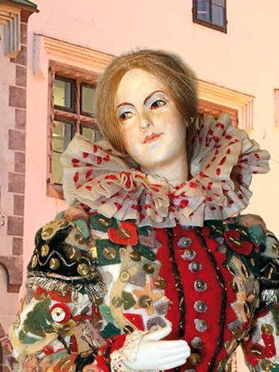 Eine kunstvolle Figur in historischer Kleidung vor einer alten Gebäudearchitektur. Die Details des Kostüms sind farbenfroh und opulent gestaltet. | © Kammerhofmuseum Bad Aussee