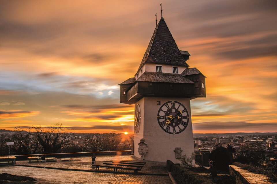 Ein schöner Ausblick auf einen alten Turm bei Sonnenuntergang. Der Himmel ist in warmen Farben gefärbt und die Stadt ist im Hintergrund sichtbar. | © Graz Tourismus - Markus Spenger