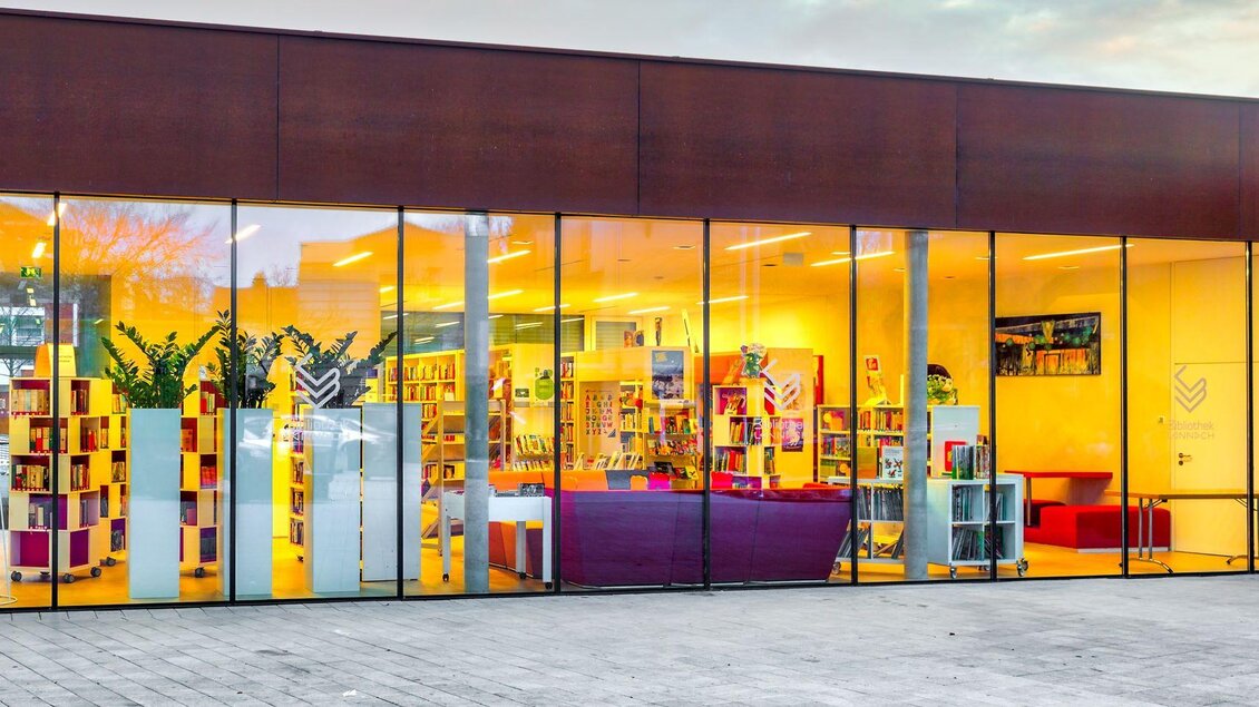 Ein modernes Gebäude mit großen Fenstern. Im Inneren sind viele Bücherregale und ein einladender Bereich zum Lesen sichtbar. | © Petru Rimovetz