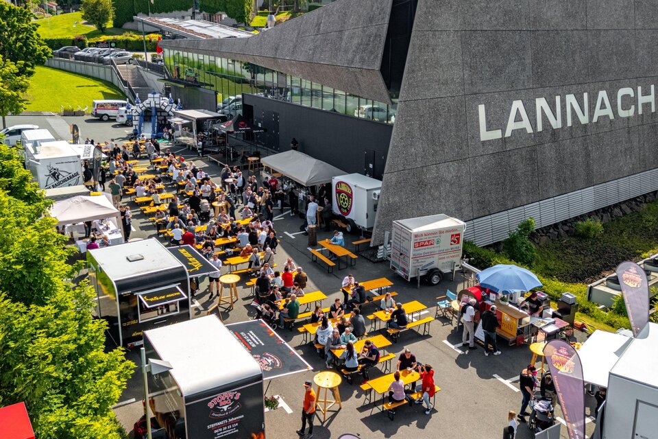 Ein belebtes Veranstaltungsgelände mit vielen Tischen und Stühlen. Food Trucks bieten verschiedene Speisen an, während die Menschen draußen genießen. | © Petru Rimovetz