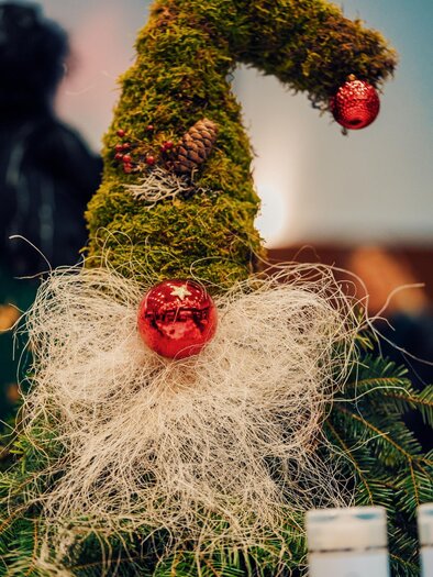 A decorative Christmas gnome made of moss with a red ornament and a white beard made of decorative material. The gnome's hat gives it a festive appearance. | © MG Lannach - Petru Rimovetz