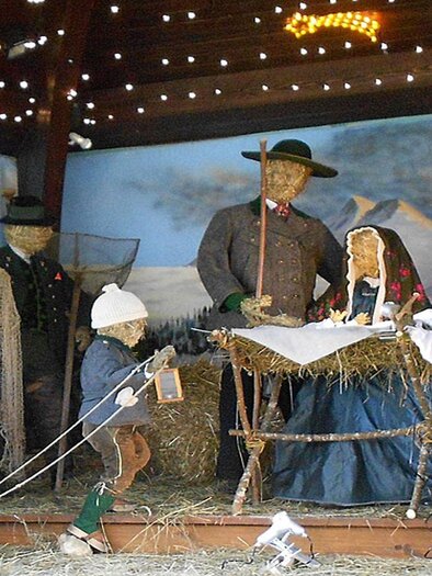 <p>Die lebensgroße Weihnachtskrippe im Musikpavillon im Gemeindepark von Grundlsee mit Figuren aus Stroh, die die heilige Familie darstellen. Die Szene zeigt auch traditionelle Handwerker und Bauern in festlicher Atmosphäre.</p> | © Hildegard Mittermair