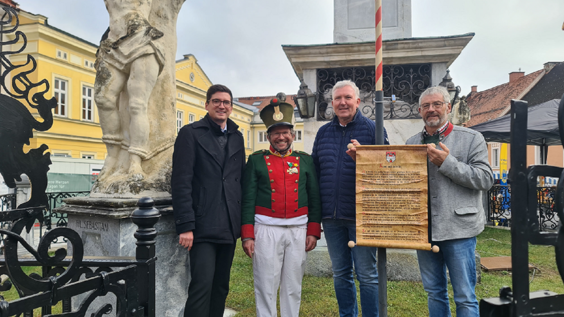 Vier Männer stehen vor einem Denkmal und lächeln in die Kamera. Einer trägt eine Uniform, während die anderen Zettel und Dokumente halten. | © TVB Murau