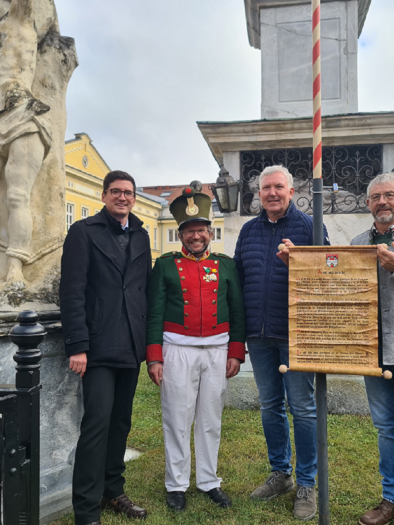 Vier Männer stehen vor einem Denkmal und lächeln in die Kamera. Einer trägt eine Uniform, während die anderen Zettel und Dokumente halten. | © TVB Murau