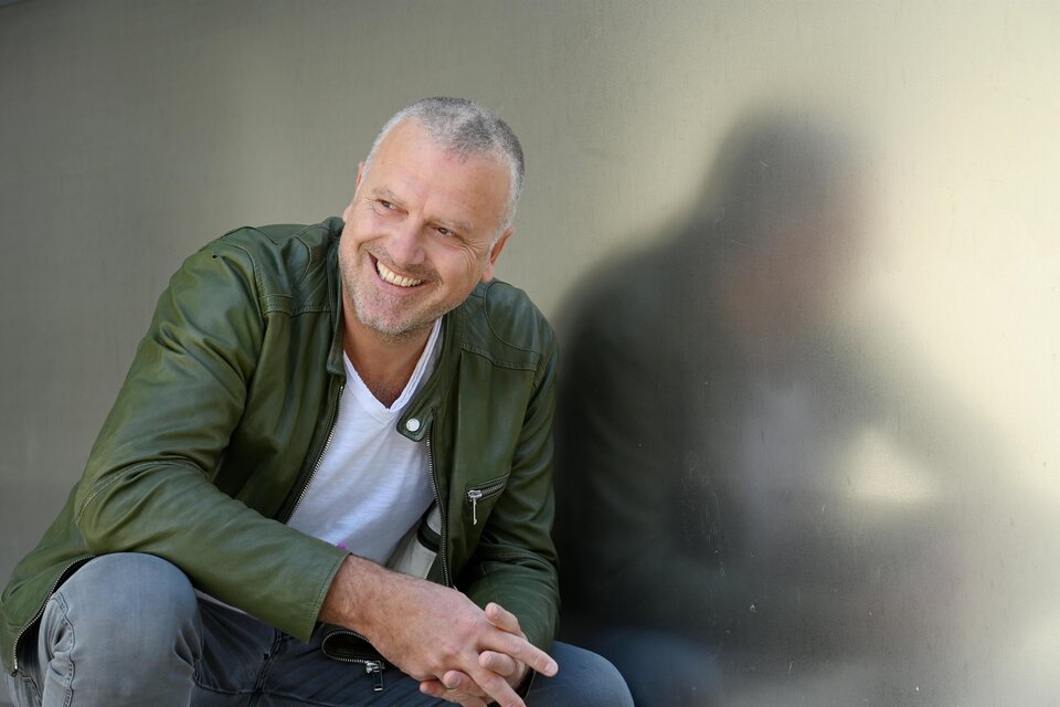 Ein lächelnder Mann sitzt an einer Wand und trägt eine grüne Jacke. Sein freundlicher Ausdruck und die entspannte Pose verleihen dem Bild eine positive Stimmung. | © Oststeiermark Tourismus