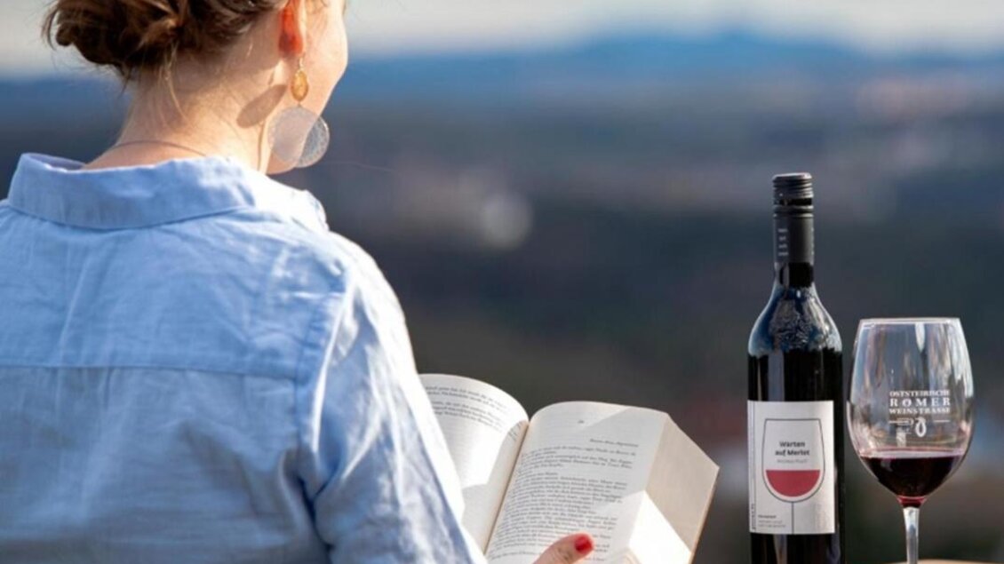 Eine Frau sitzt im Freien und liest ein Buch. Neben ihr stehen eine Flasche Wein und ein Glas Wein, mit schöner Landschaft im Hintergrund. | © Weingut Posch