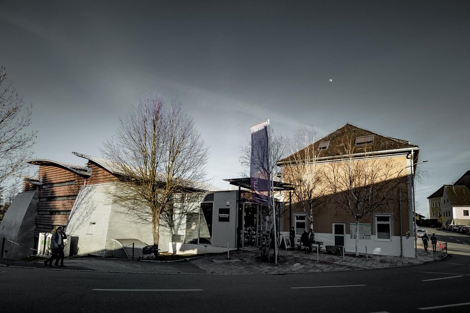 Ein modernes Gebäude mit einer ungewöhnlichen Architektur steht an einer Straße. Im Hintergrund ist eine traditionelle Kirche zu sehen. | © Ulrike_Rauch