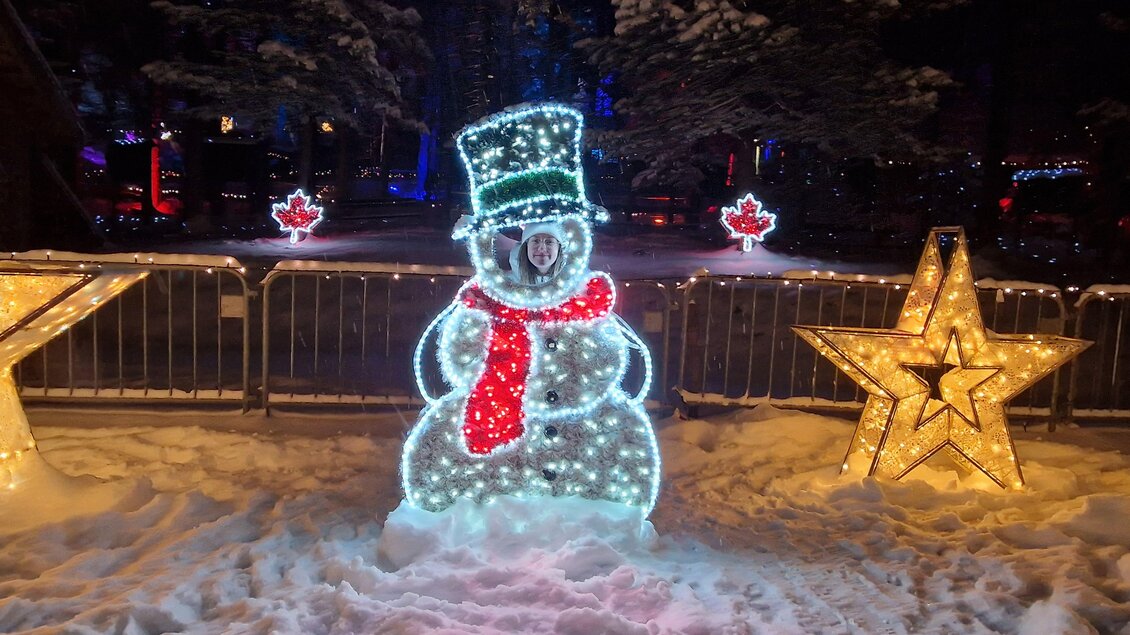 Ein leuchtender Schneemann mit einem grünen Hut und rotem Schal steht im Schnee. Um ihn herum sind dekorative Sterne und winterliche Lichter. | © Mariazeller Bürgeralpe