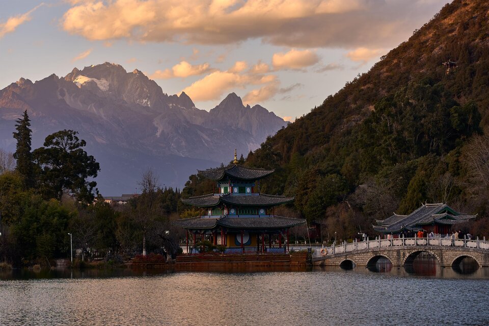 Eine Aussicht auf einen malerischen Tempel am Wasser, umgeben von Bergen und Bäumen. Der Himmel ist bei Sonnenuntergang in warmen Farben beleuchtet. | © Michael Fischer