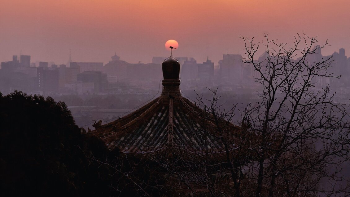 Ein schöner Sonnenuntergang über einer traditionellen Dachstruktur. Die Silhouette der Stadt ist im Hintergrund zu sehen. | © Michael Fischer