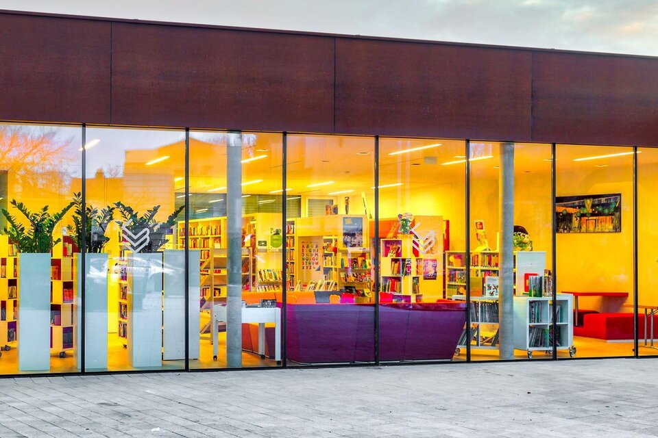 Ein modernes Gebäude mit großen Fenstern. Im Inneren sind viele Bücherregale und ein einladender Bereich zum Lesen sichtbar. | © Petru Rimovetz