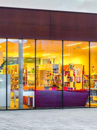 Ein modernes Gebäude mit großen Fenstern. Im Inneren sind viele Bücherregale und ein einladender Bereich zum Lesen sichtbar. | © Petru Rimovetz