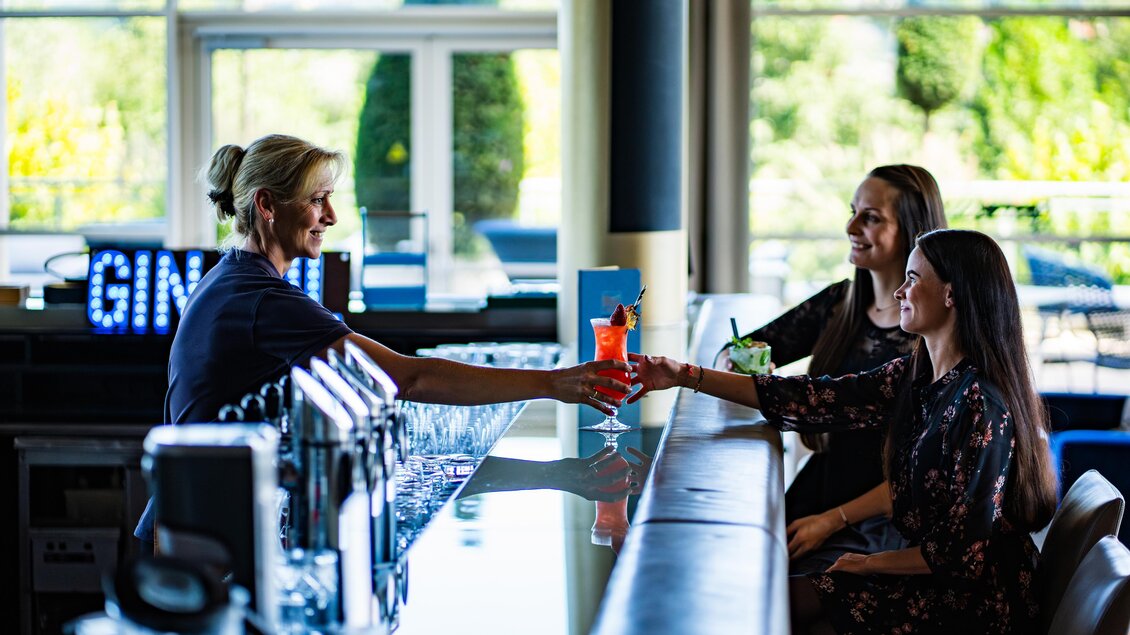 <p><p>Eine Barkeeperin serviert Cocktails an zwei Gäste an der Bar. Die Atmosphäre ist freundlich und entspannt im SPA RESORT STYRIA.</p></p> | © SPA Resort Styria