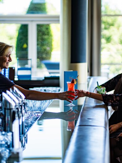 <p><p>A bartender serves cocktails to two guests at the bar. The atmosphere is friendly and relaxed at the SPA RESORT STYRIA.</p></p> | © SPA Resort Styria