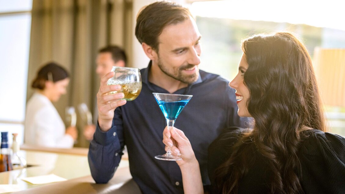 <p>Ein Paar genießt Drinks in einer stilvollen Bar. Sie lachen und stoßen mit ihren Gläsern an im SPA RESORT STYRIA.</p>