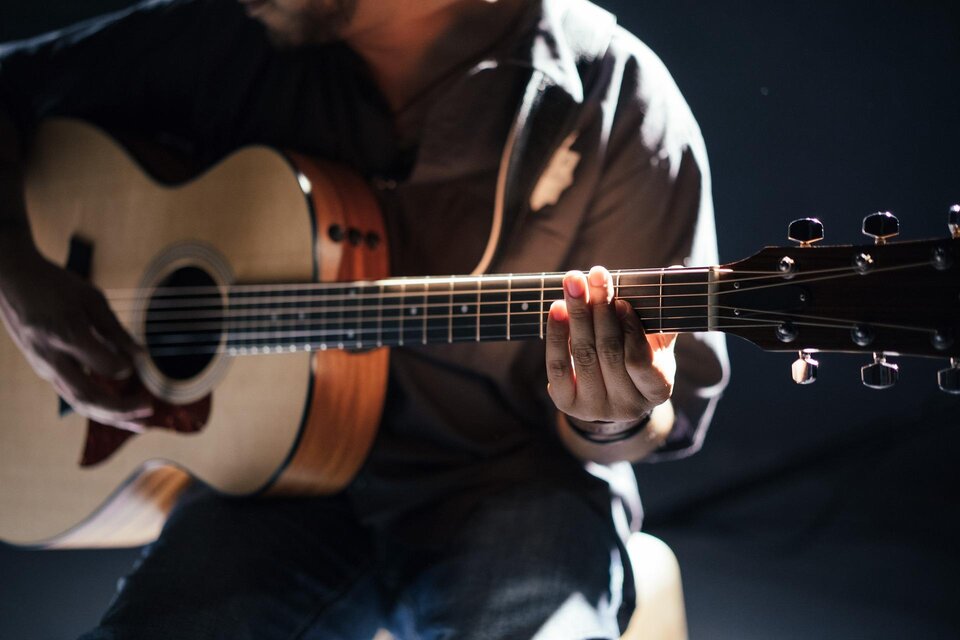 Ein Musiker spielt eine Akustikgitarre. Die Hände sind auf dem Hals der Gitarre und die Beleuchtung ist sanft. | © Pixabay