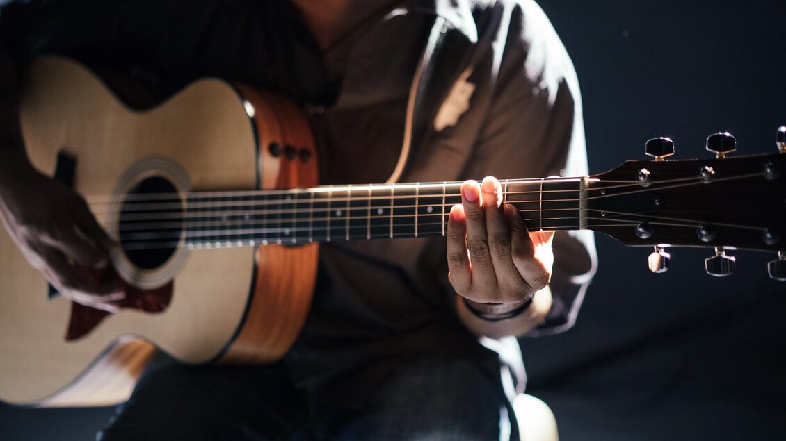 Ein Musiker spielt eine Akustikgitarre. Die Hände sind auf dem Hals der Gitarre und die Beleuchtung ist sanft. | © Pixabay