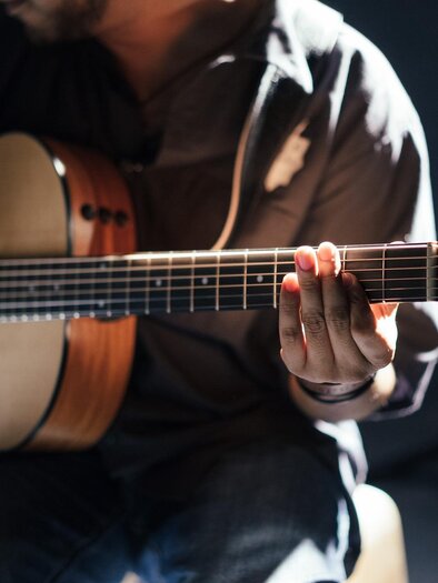 A musician is playing an acoustic guitar. The hands are on the neck of the guitar and the lighting is soft. | © Pixabay