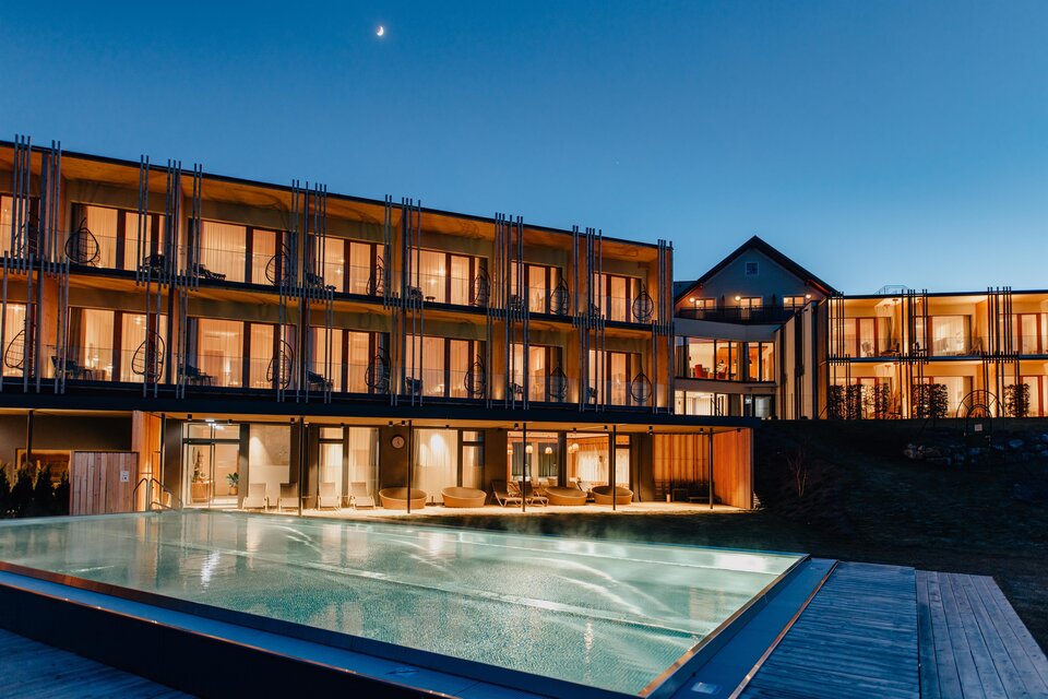 Ein modernes Hotelgebäude mit vielen Fenstern und einem großen Pool. Die Szene zeigt einen klaren Abendhimmel mit einem Hauch von Dämmerung. | © Karin Bergmann