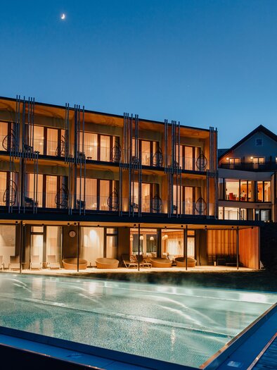 Ein modernes Hotelgebäude mit vielen Fenstern und einem großen Pool. Die Szene zeigt einen klaren Abendhimmel mit einem Hauch von Dämmerung. | © Karin Bergmann