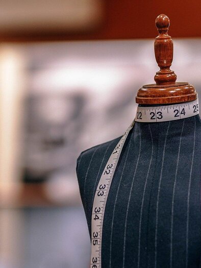 A dress form with a measuring tape around its neck stands in the foreground. The background is blurred and shows a creative environment. | © Pixabay