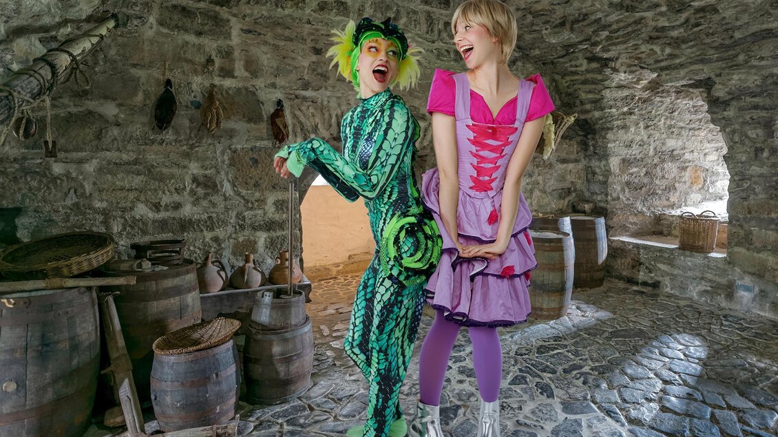 Zwei verkleidete Darsteller als Rapunzel und Geko in einem historischen Burgkeller mit Steinwänden und Holzfässern in Graz. | © Märchensommer-Martin Hesz