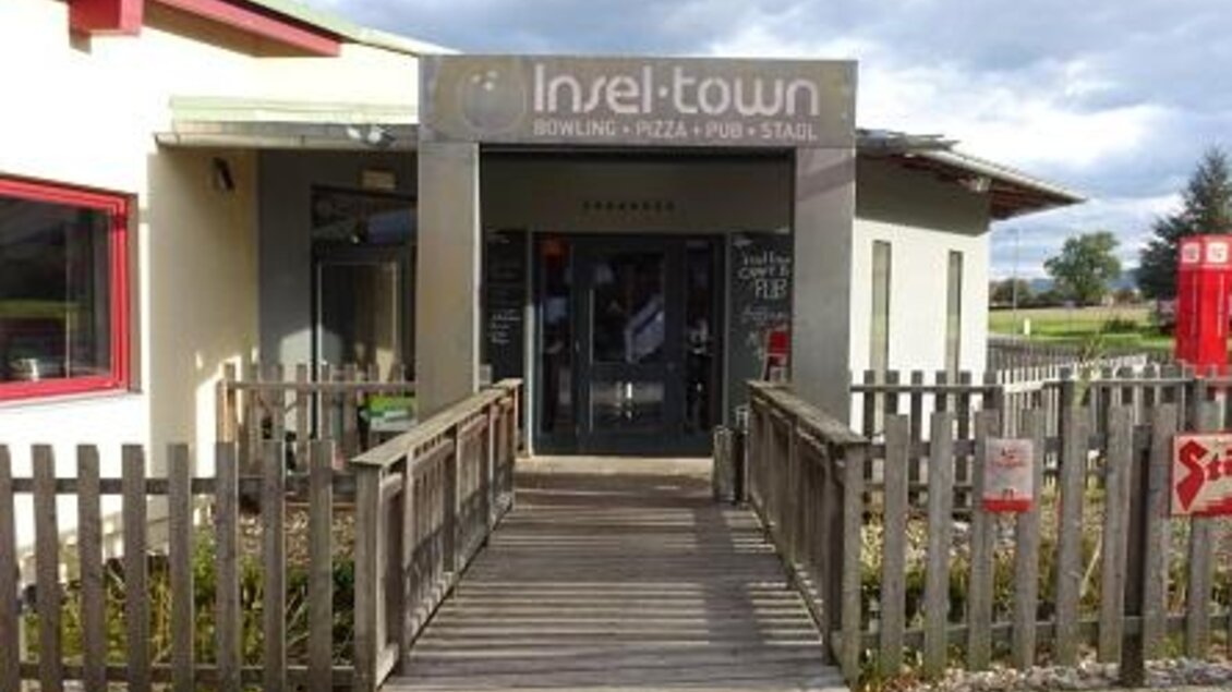 Ein Eingangsbereich zu "Insel-town" mit einer Holzbrücke und einem modernen Gebäude. Es bietet Bowling, Pizza und eine Bar. | © Inseltown