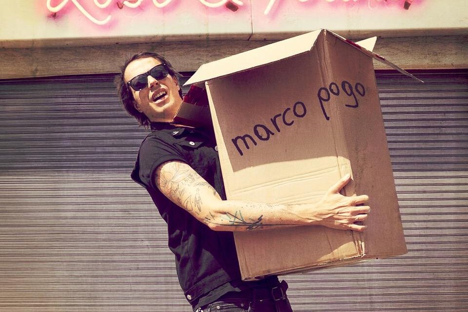 Ein Mann mit Sonnenbrille hält einen großen Karton mit der Aufschrift "marco pogo". Im Hintergrund leuchtet ein Schild mit "Lost & Found". | © pogogsempire