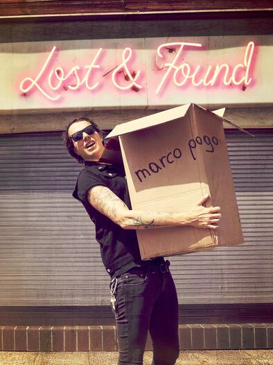 Ein Mann mit Sonnenbrille hält einen großen Karton mit der Aufschrift "marco pogo". Im Hintergrund leuchtet ein Schild mit "Lost & Found". | © pogogsempire