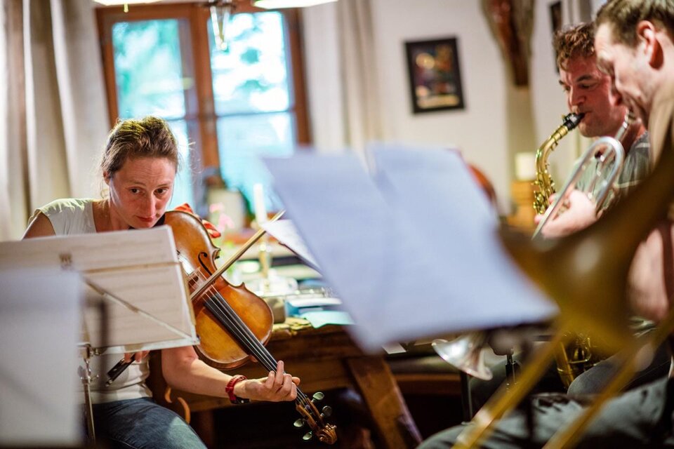 Eine Musikergruppe spielt in einem gemütlichen Raum. Im Vordergrund spielt eine Frau mit einer Violine. | © @Greith Haus