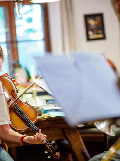 A group of musicians is playing in a cozy room. In the foreground, a woman is playing a violin. | © @Greith Haus