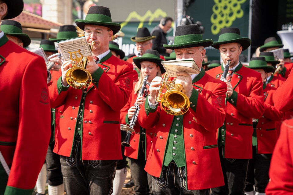 Eine Gruppe von Musikern trägt rote Jacken und schwarze Hüte. Sie spielen traditionelle Instrumente bei einem Festumzug. | © Ekatarina Paller