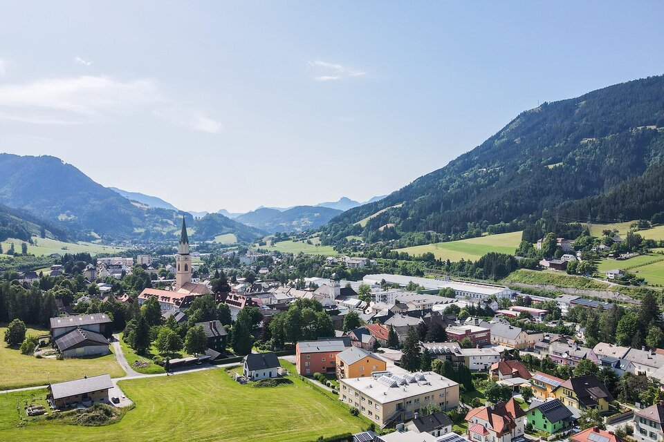 Eine malerische Berglandschaft mit einem kleinen Dorf. Die grünen Wiesen und die Berge im Hintergrund schaffen eine idyllische Atmosphäre.