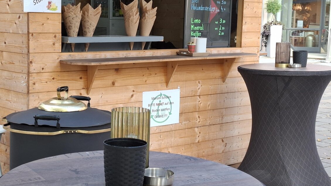 Ein kleiner Imbissstand aus Holz mit einem Fenster und verschiedenen Snacks. Draußen stehen zwei Tische und eine Mülleimer. | © Gerlinde Rath