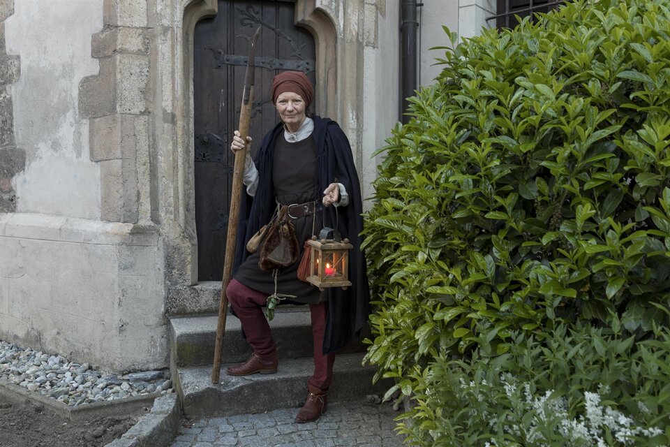 Ein mittelalterlicher Mann steht vor einer Tür und hält eine Laterne in der Hand. Er trägt traditionelle Kleidung und hat einen Gehstock dabei. | © Martin Meieregger